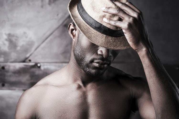 Wearing his favorite hat. Portrait of young shirtless African man adjusting his hat while standing against metal background