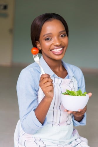 attractive african woman eating fresh green salad at home