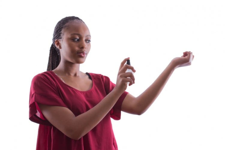African woman with braids in a red shirt is trying a new perfume on an isolated white background