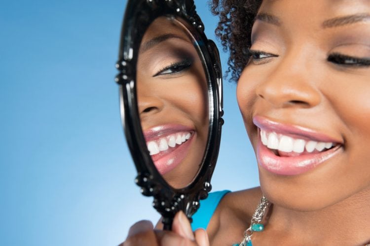 Close-up of a young woman looking at herself in mirror and smiling over colored background